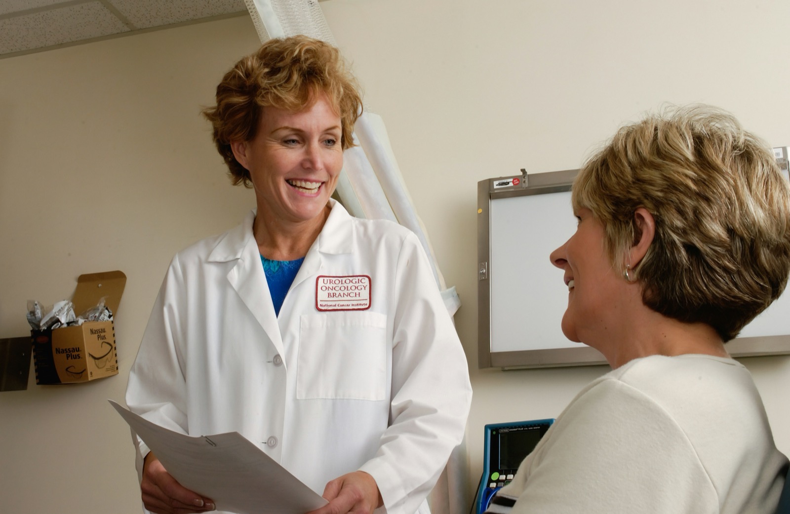 A clinician in scrubs holding a laptop during a consultation.