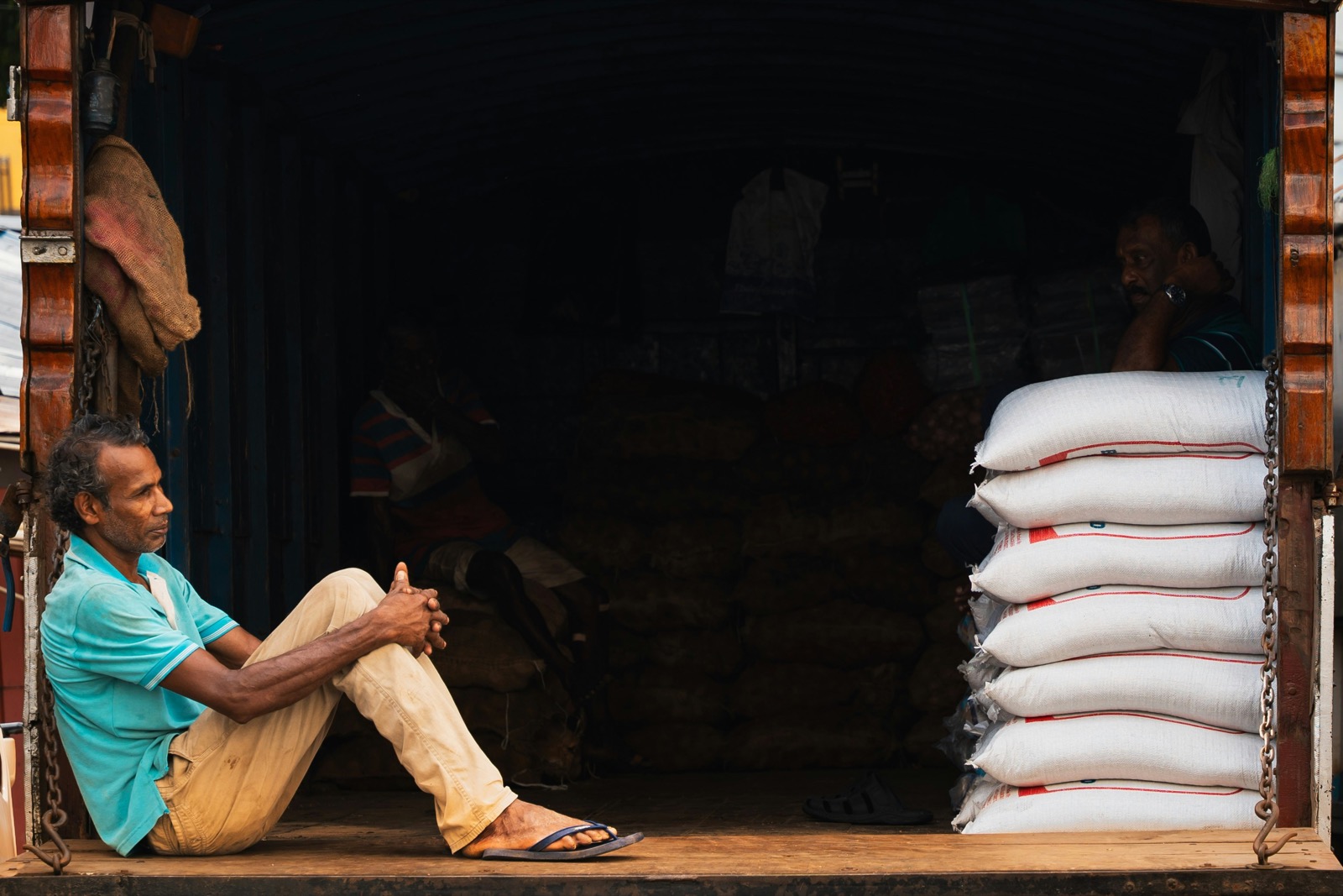 A loader resting on the tailgate of a truck stacked with sacks of grain.
