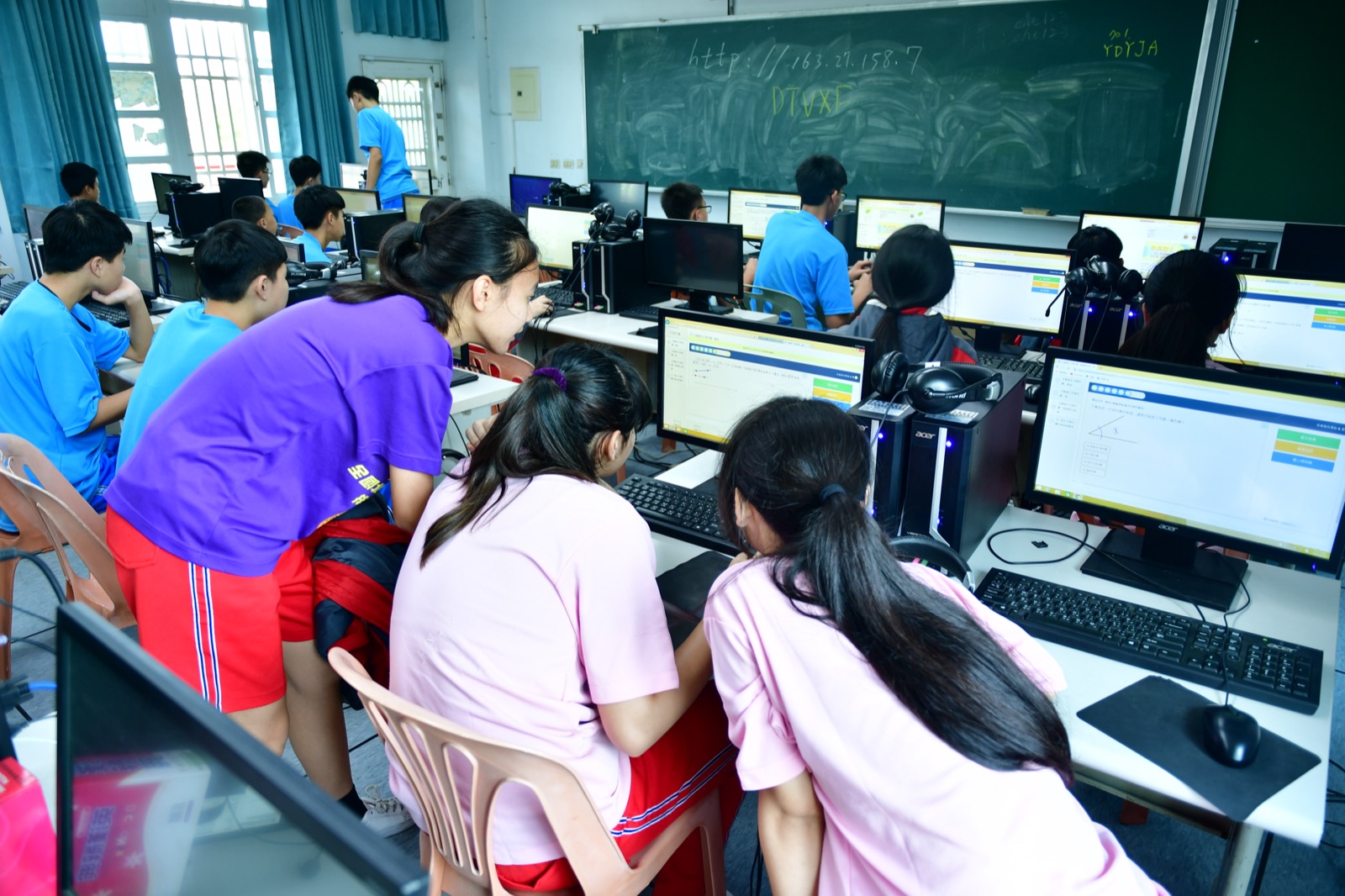 A junior high computer classroom, students working through an on-screen exercise at desktop machines.